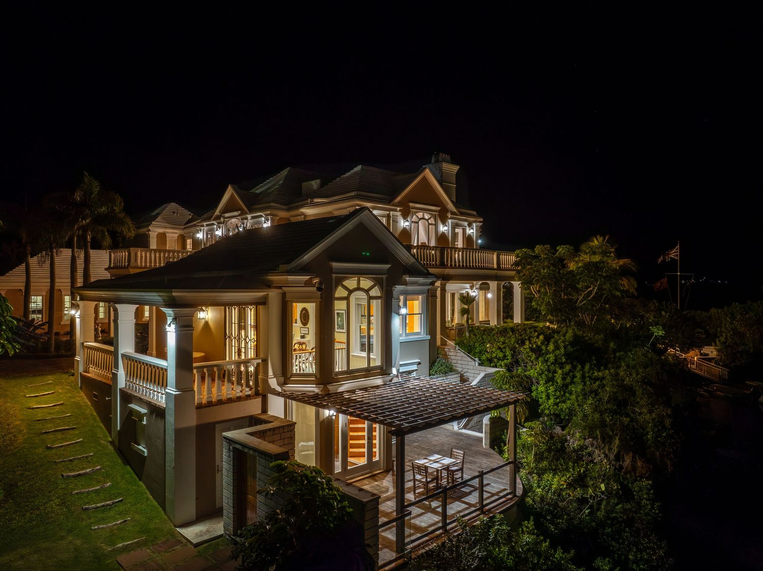 Modern luxury home with illuminated outdoor living spaces and ocean views at night. Drone photogrpahy.