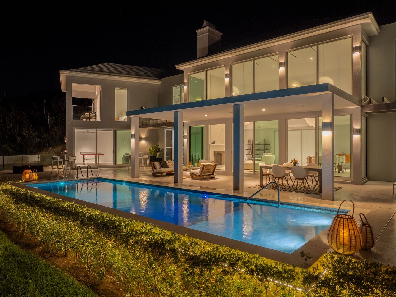 Modern oceanfront property with glass walls and infinity pool glowing at twilight.