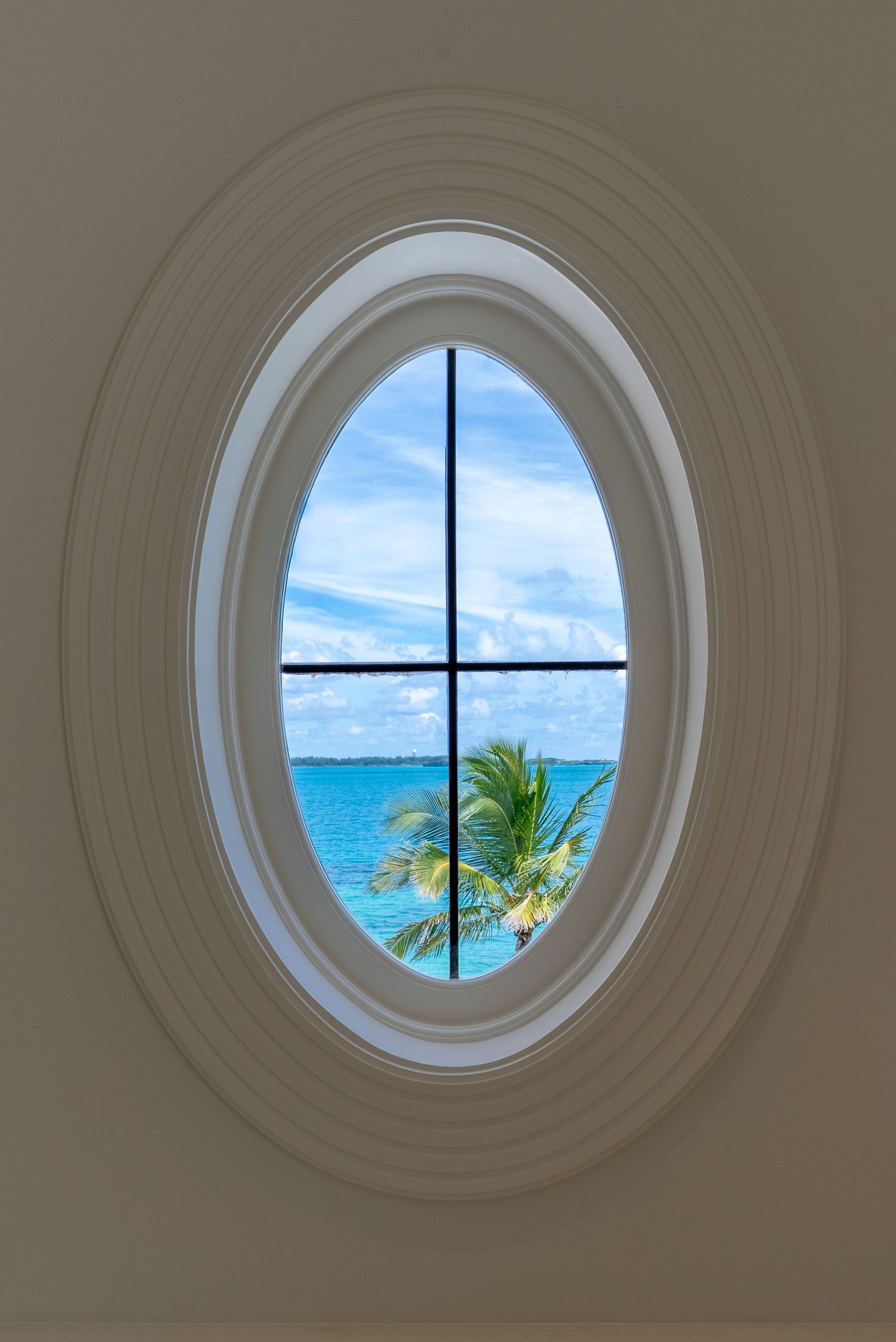 Circular window with ocean view framing tropical palm trees and turquoise waters against blue sky.