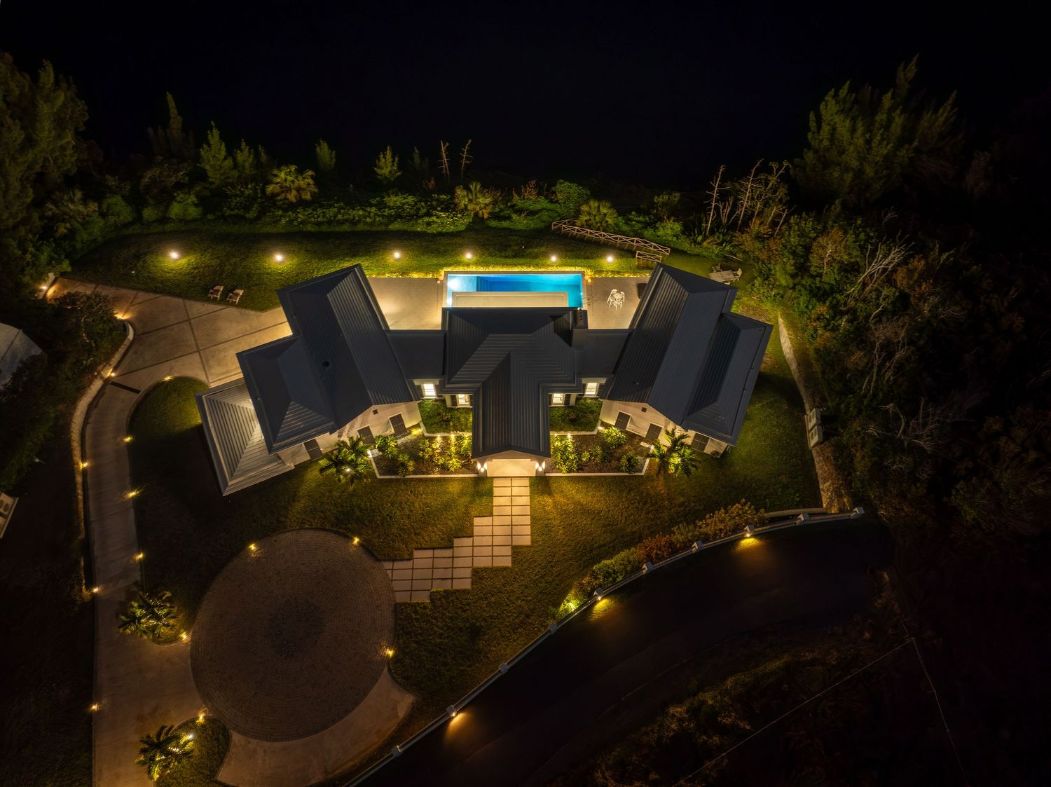 Aerial nighttime view of a luxurious waterfront estate with illuminated landscaping and pool. Drone photogrpahy.