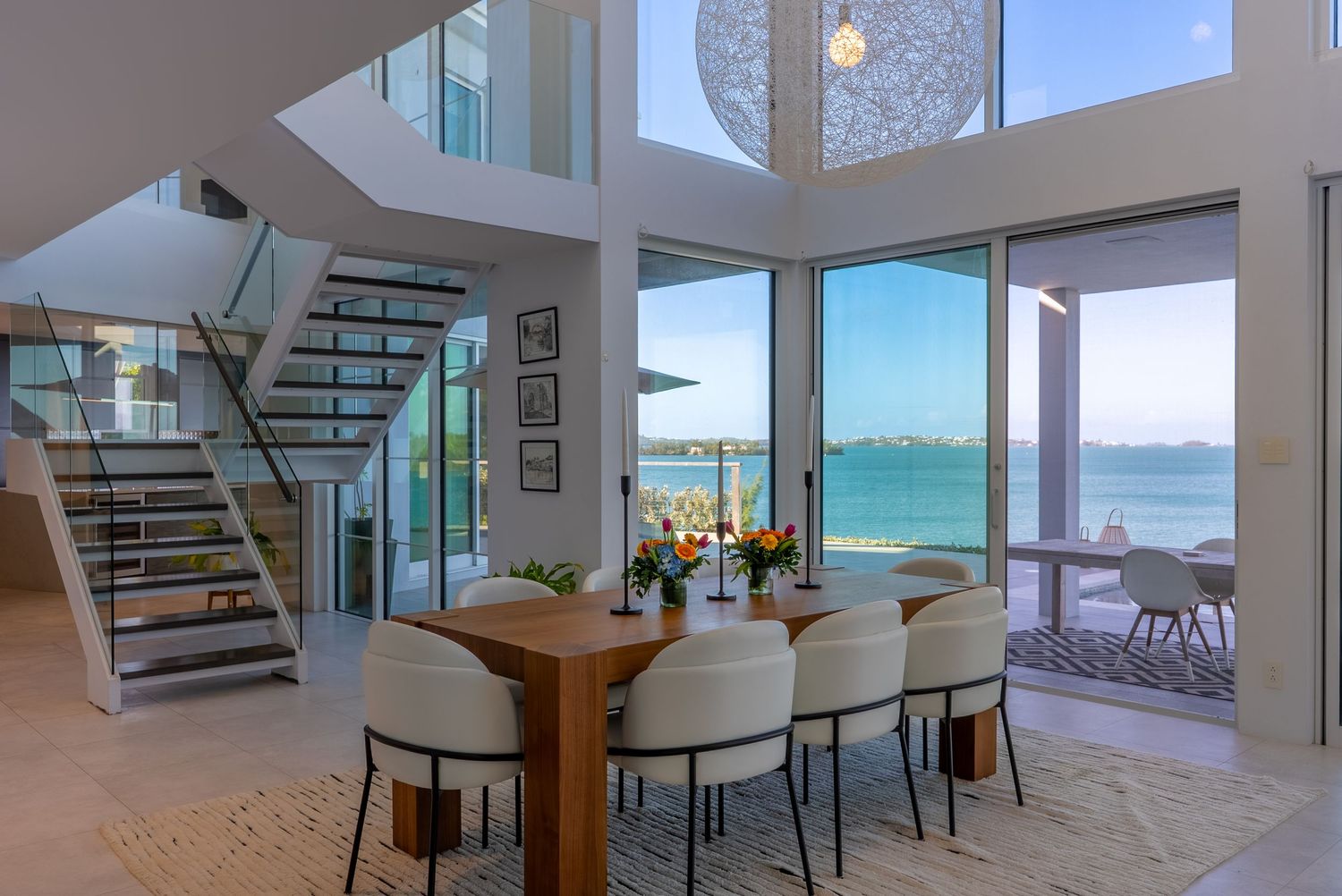 Contemporary dining and living area with floating staircase and panoramic ocean views.