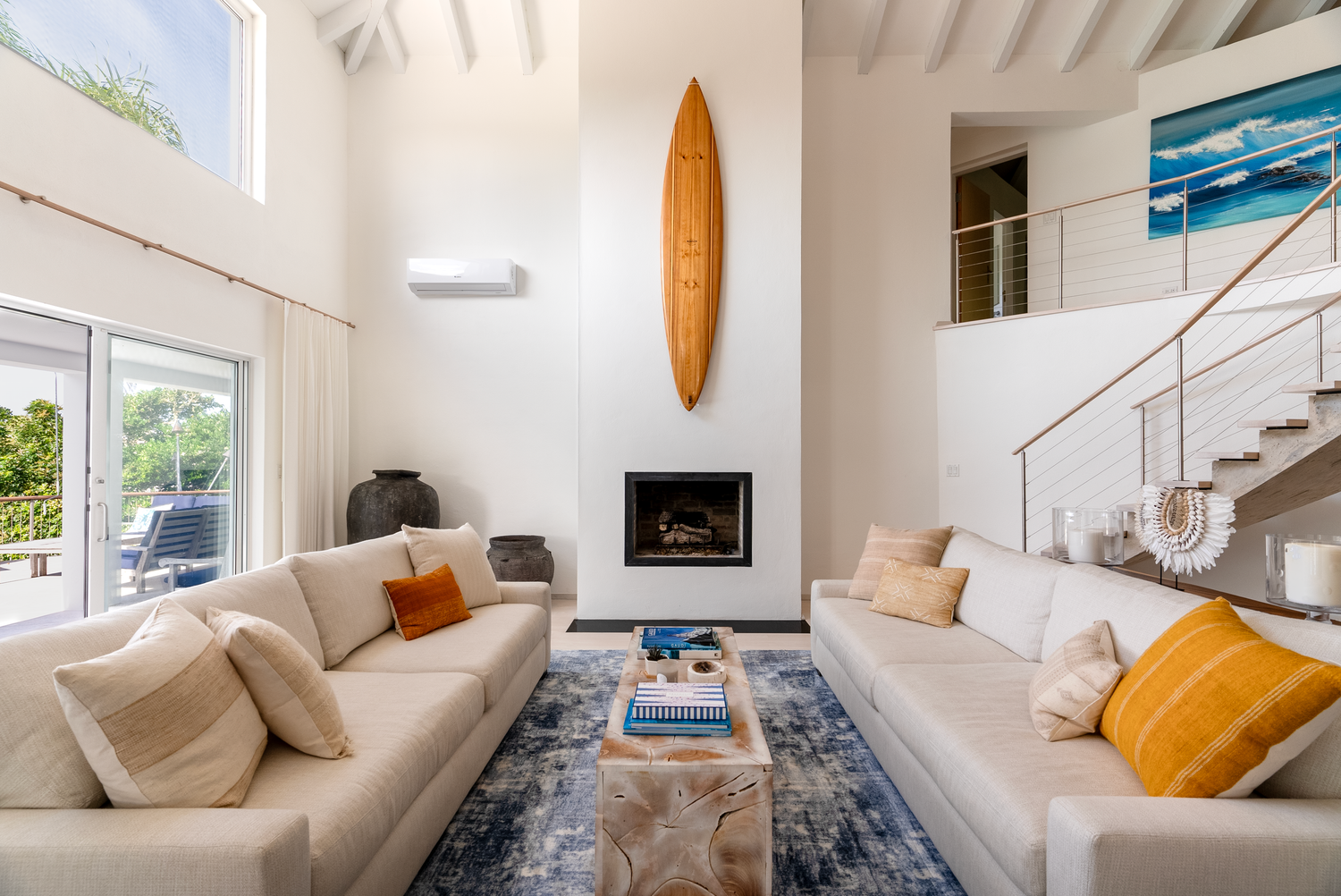 Modern white living room with vaulted ceiling, surfboard decor, and coastal views.