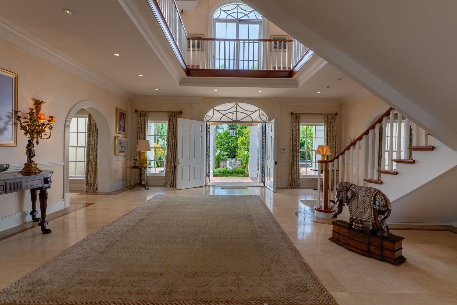 Grand foyer with sweeping staircase, arched windows, and polished marble floors in an elegant mansion.