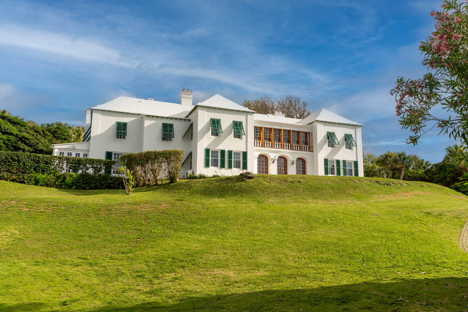 Rolling green hills with white luxury homes nestled along the coastline under blue skies.