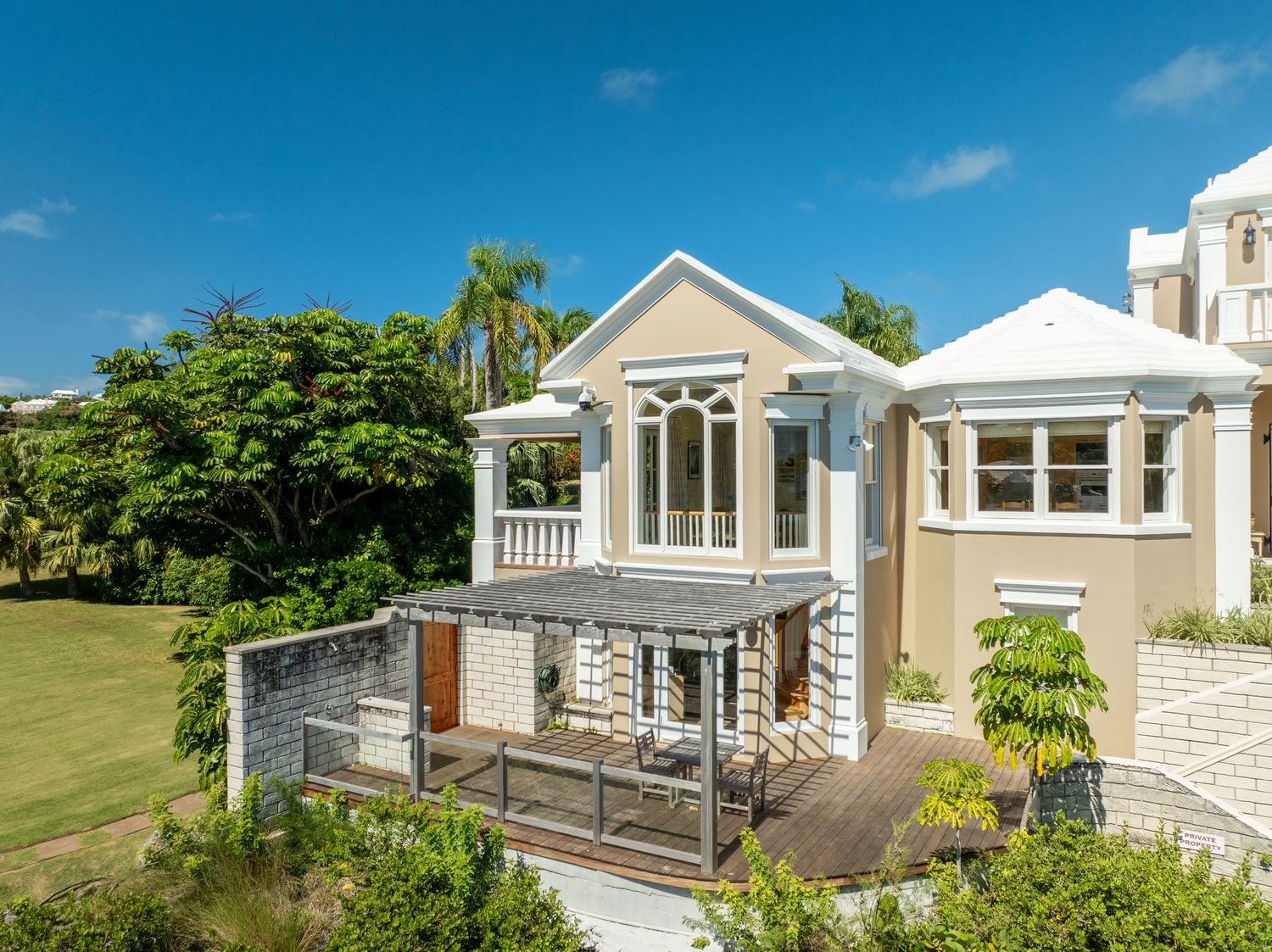 Elegant coastal mansion with white exterior and wraparound porch overlooking tropical gardens. Drone photogrpahy.