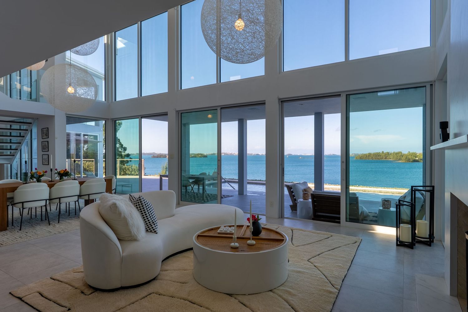 Luxurious oceanfront living room with curved windows and modern white furniture.