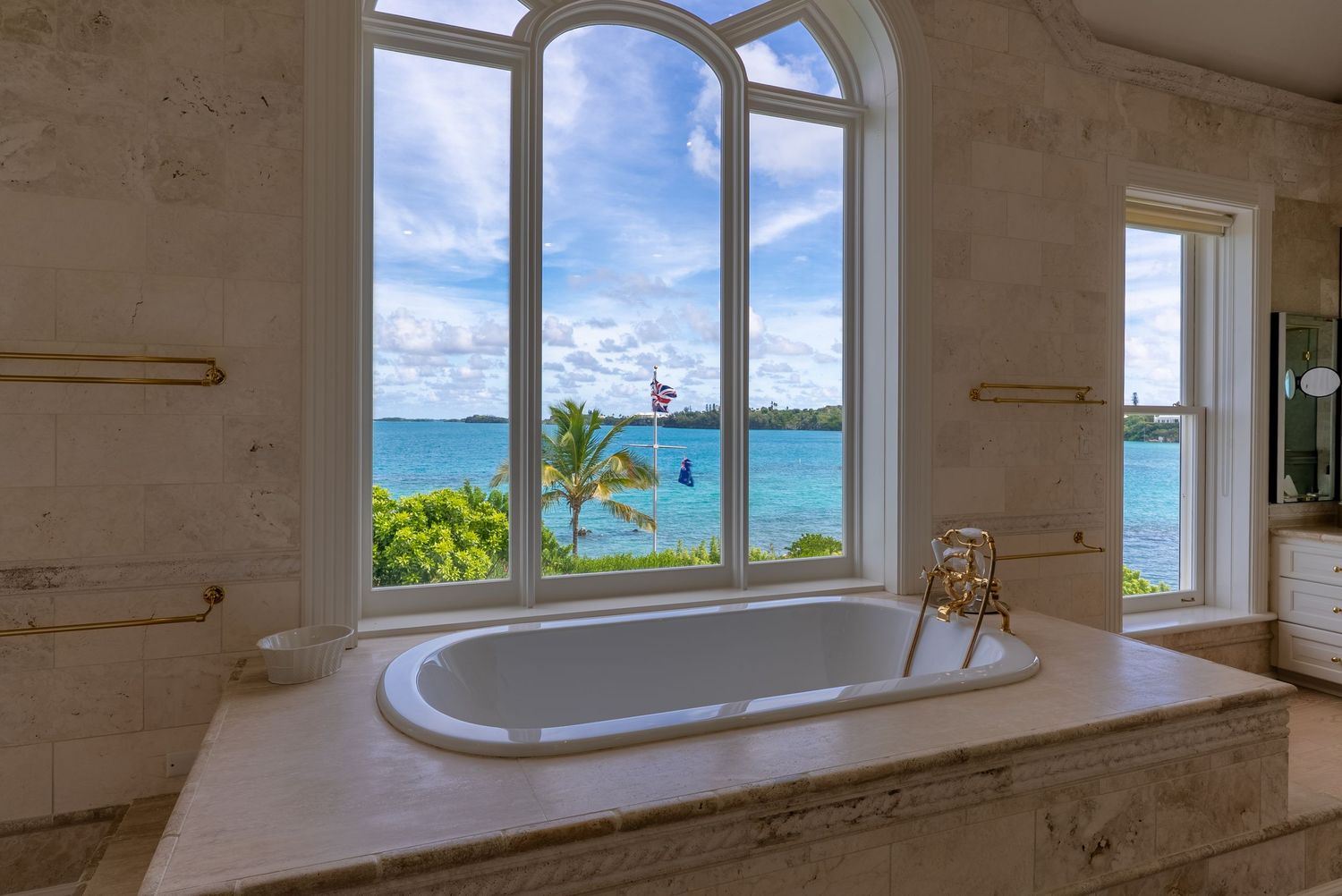 Luxury bathroom with freestanding tub overlooking ocean views through large arched windows.