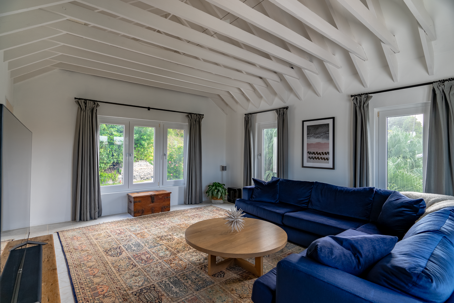 Spacious bedroom with exposed beam ceiling, ocean views, and modern blue furnishings.