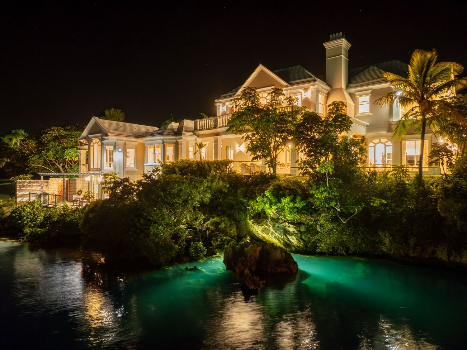 Waterfront luxury residence with glowing turquoise pool and architectural lighting at dusk. Drone photogrpahy.