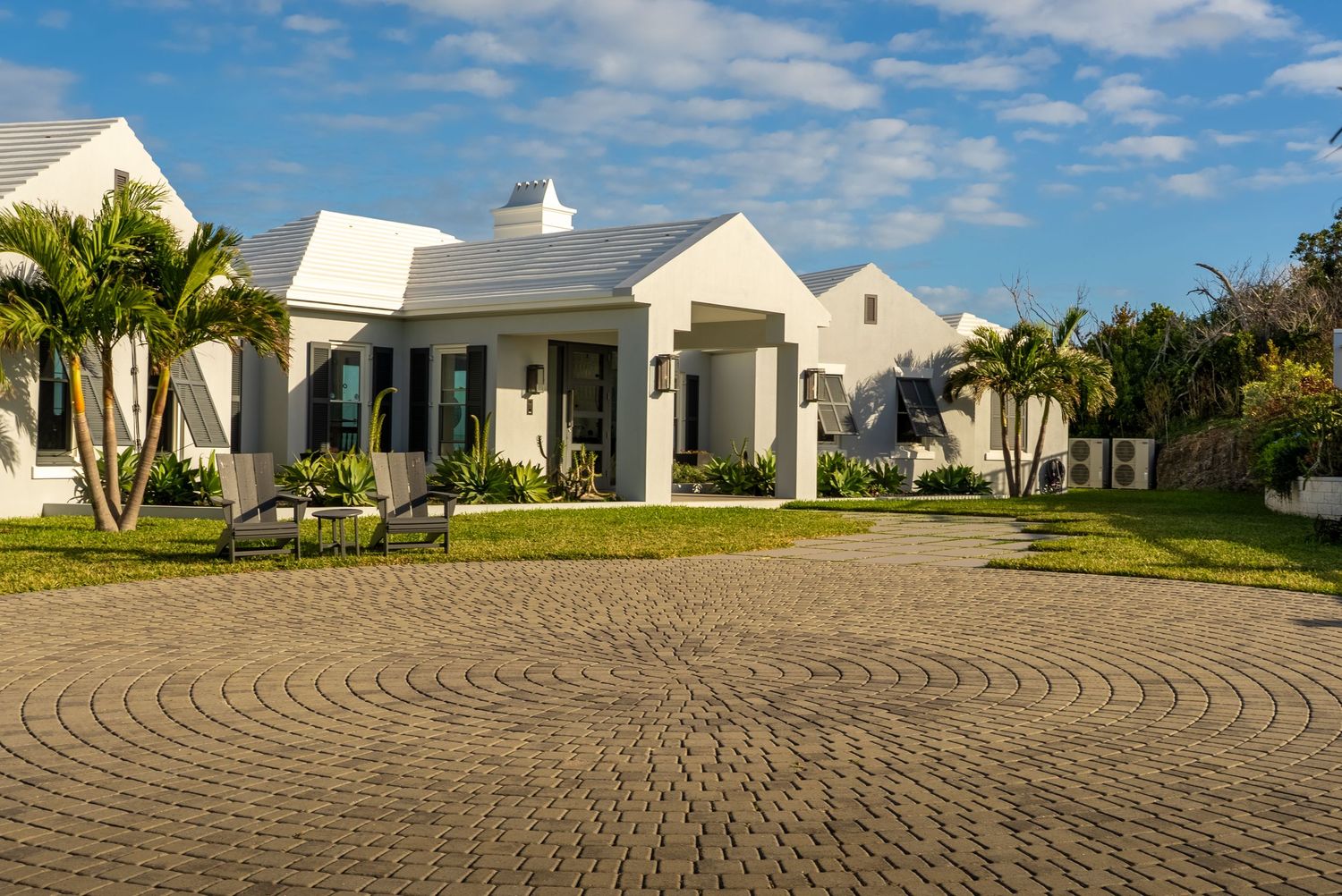 Circular paved driveway leading to elegant white coastal homes with manicured grounds.