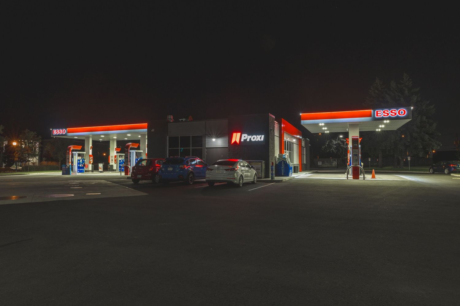 Illuminated gas station convenience store glows brightly against dark night sky with red signage visible.