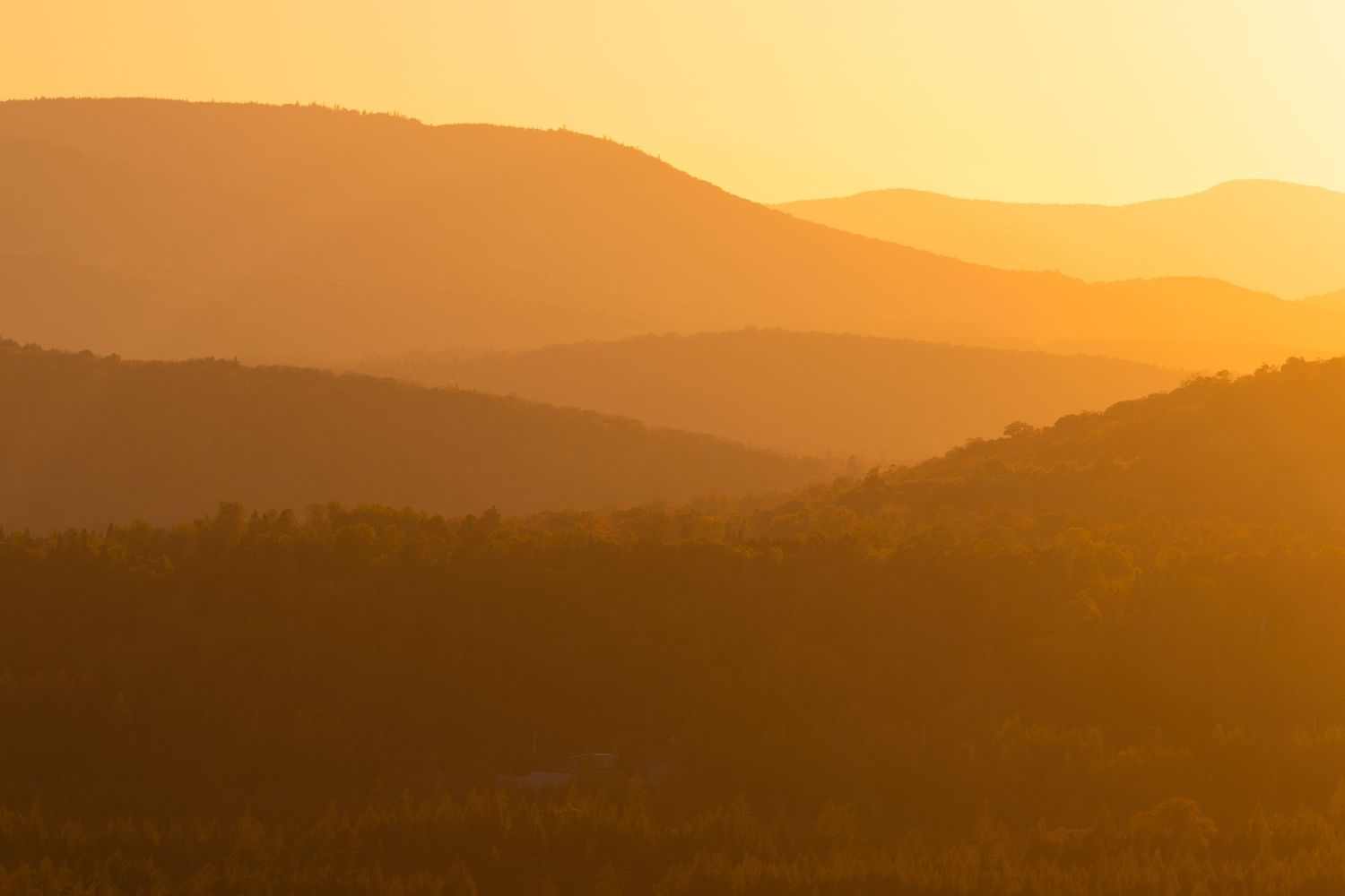 Silhouetted mountain ranges at sunset creating layers of golden orange gradients.