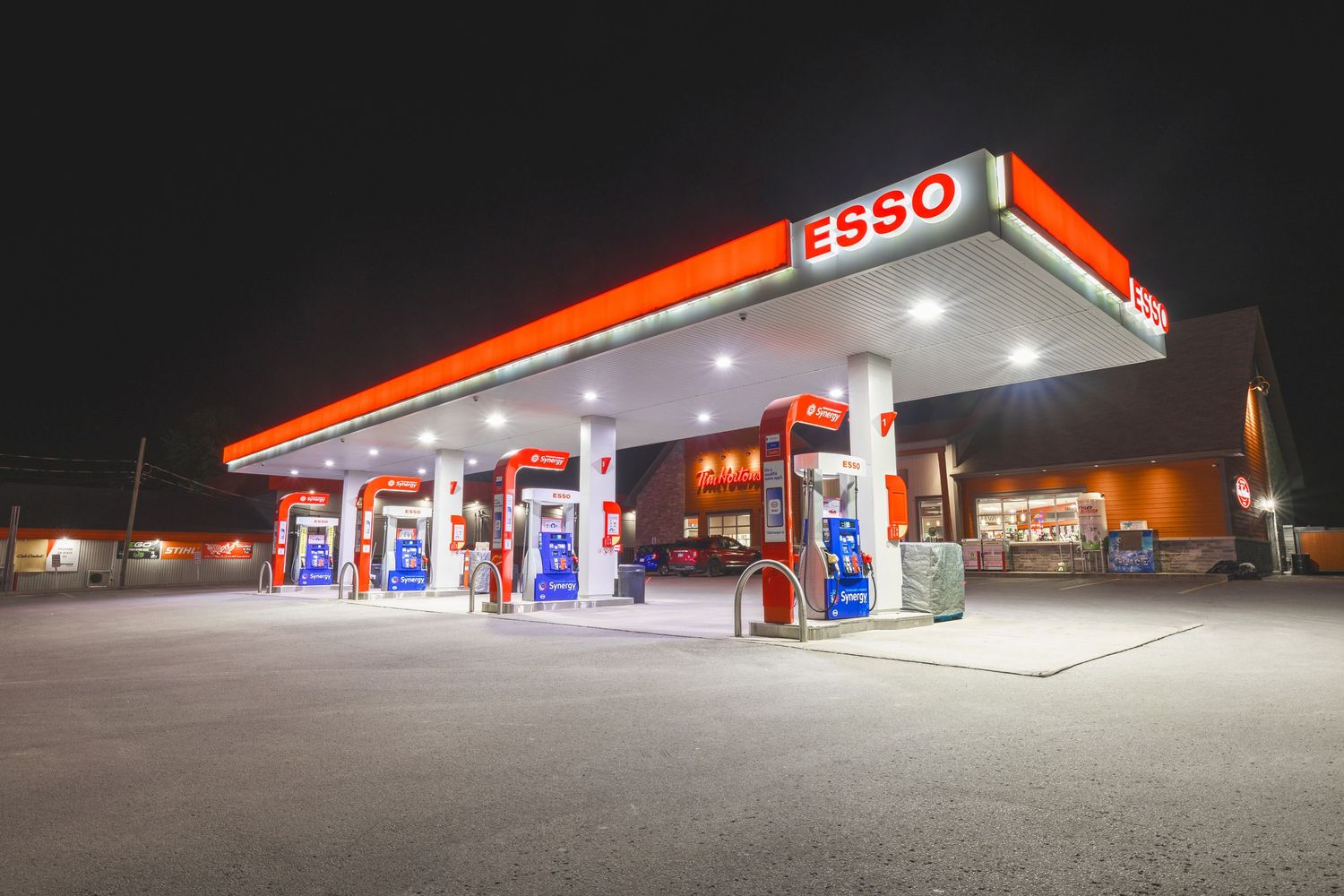 Illuminated Esso gas station with bright orange canopy glows against dark night sky at multiple angles.