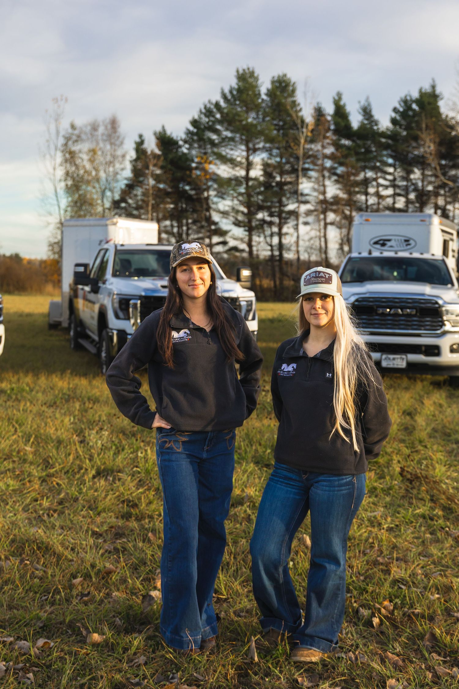 People standing in casual attire against backdrop of parked vehicles in field.