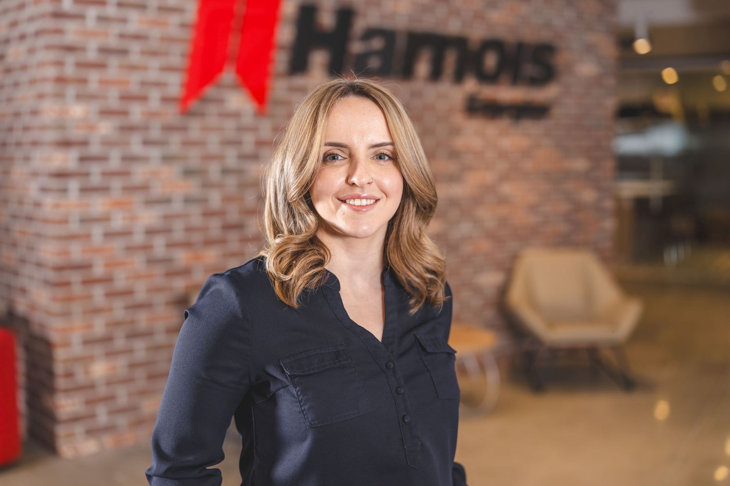 Professional headshot against brick wall with red company branding visible.
