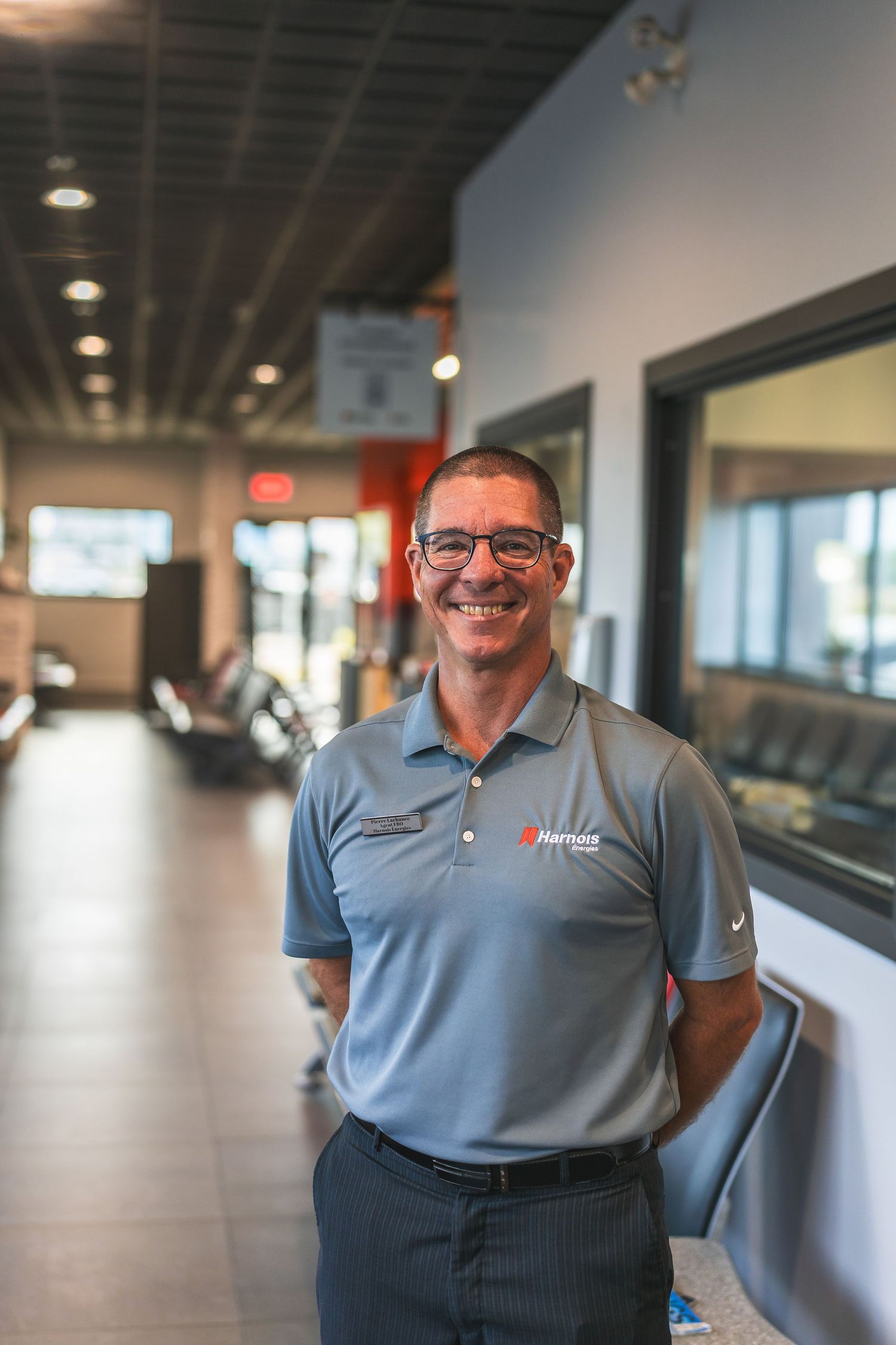 Professional in grey polo shirt standing in modern office hallway.
