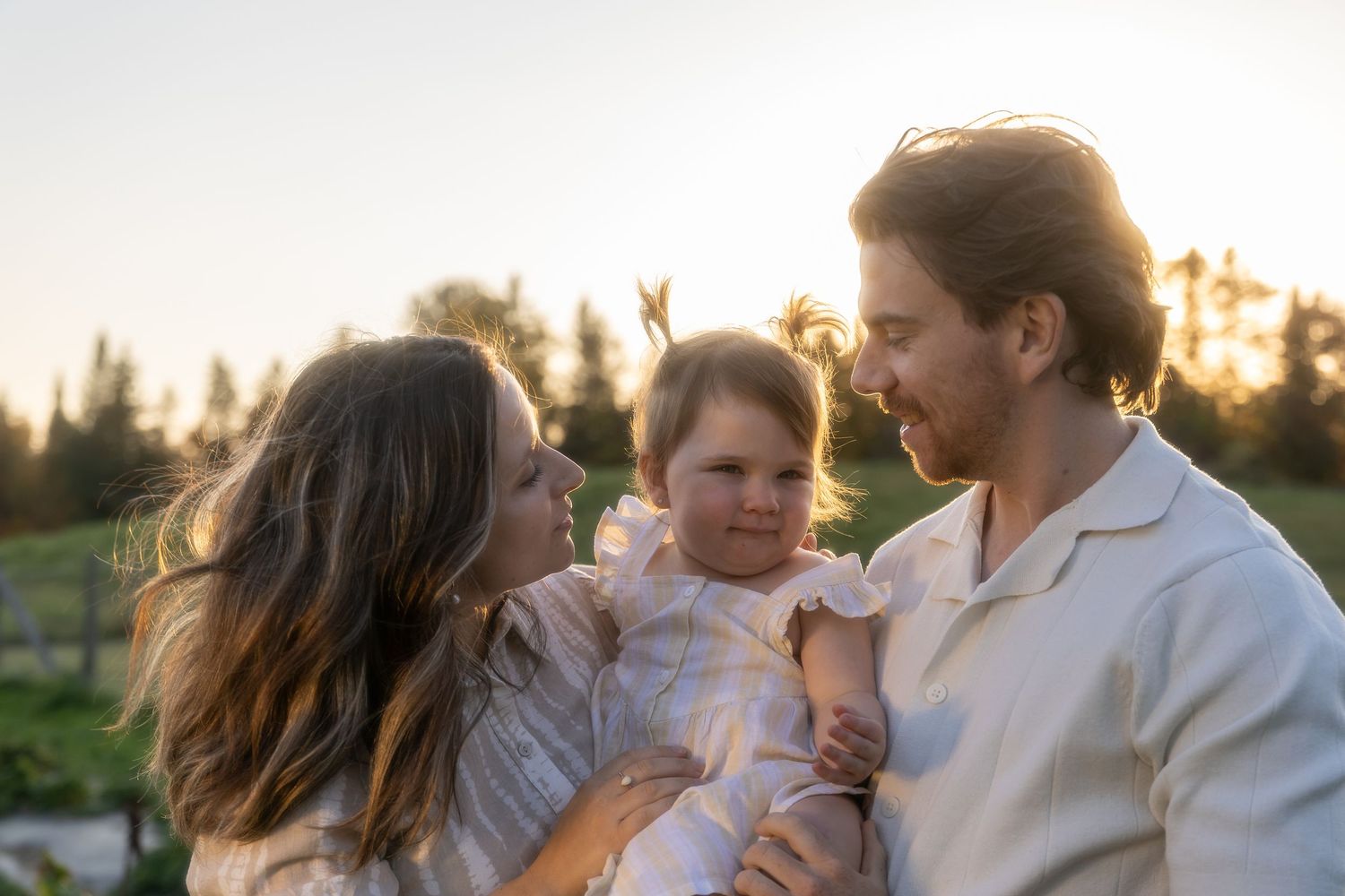 Family embracing outdoors during sunset in casual white clothing.