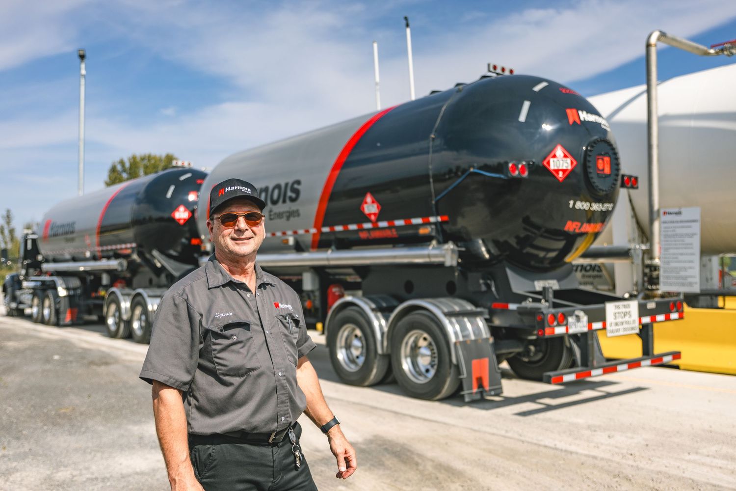 Worker stands beside large industrial fuel tanker trucks in outdoor facility.
