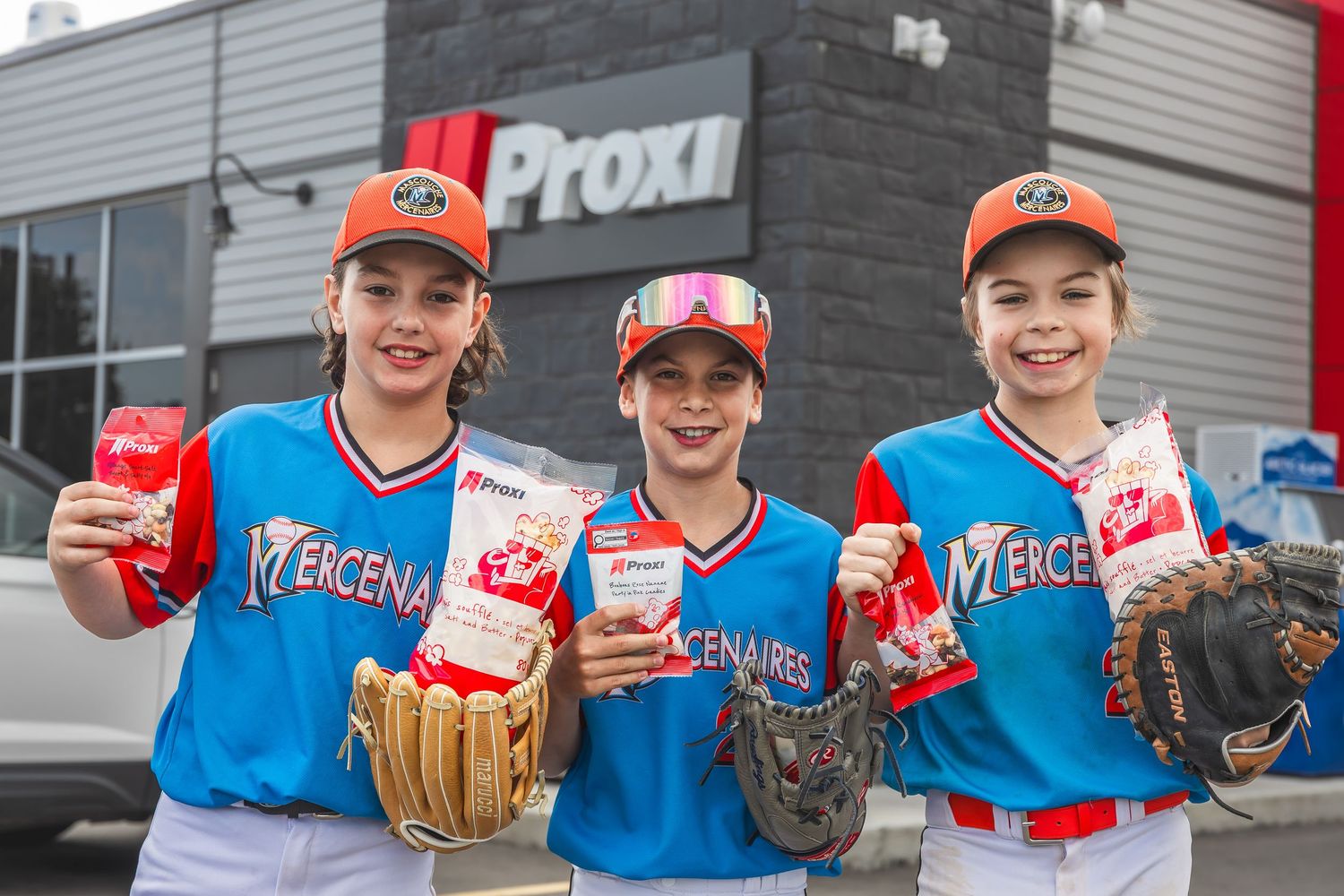 Three baseball players in bright blue uniforms pose with gloves and Coca-Cola drinks outside a building.
