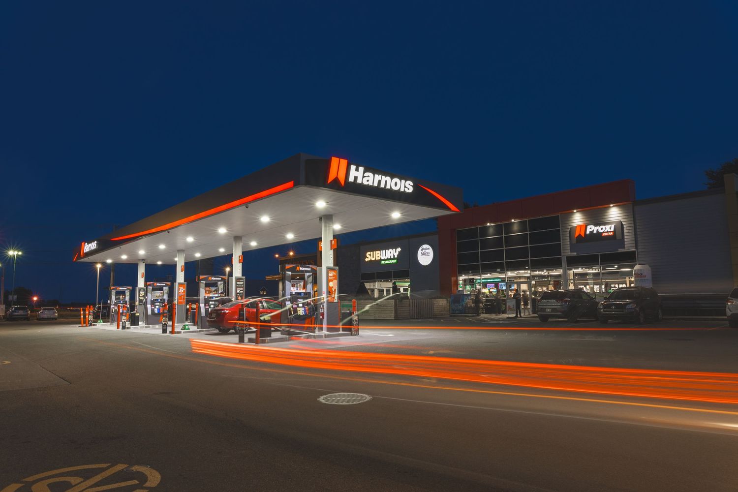 A nighttime view of a Hamon gas station with bright orange accents illuminated against a dark blue sky.