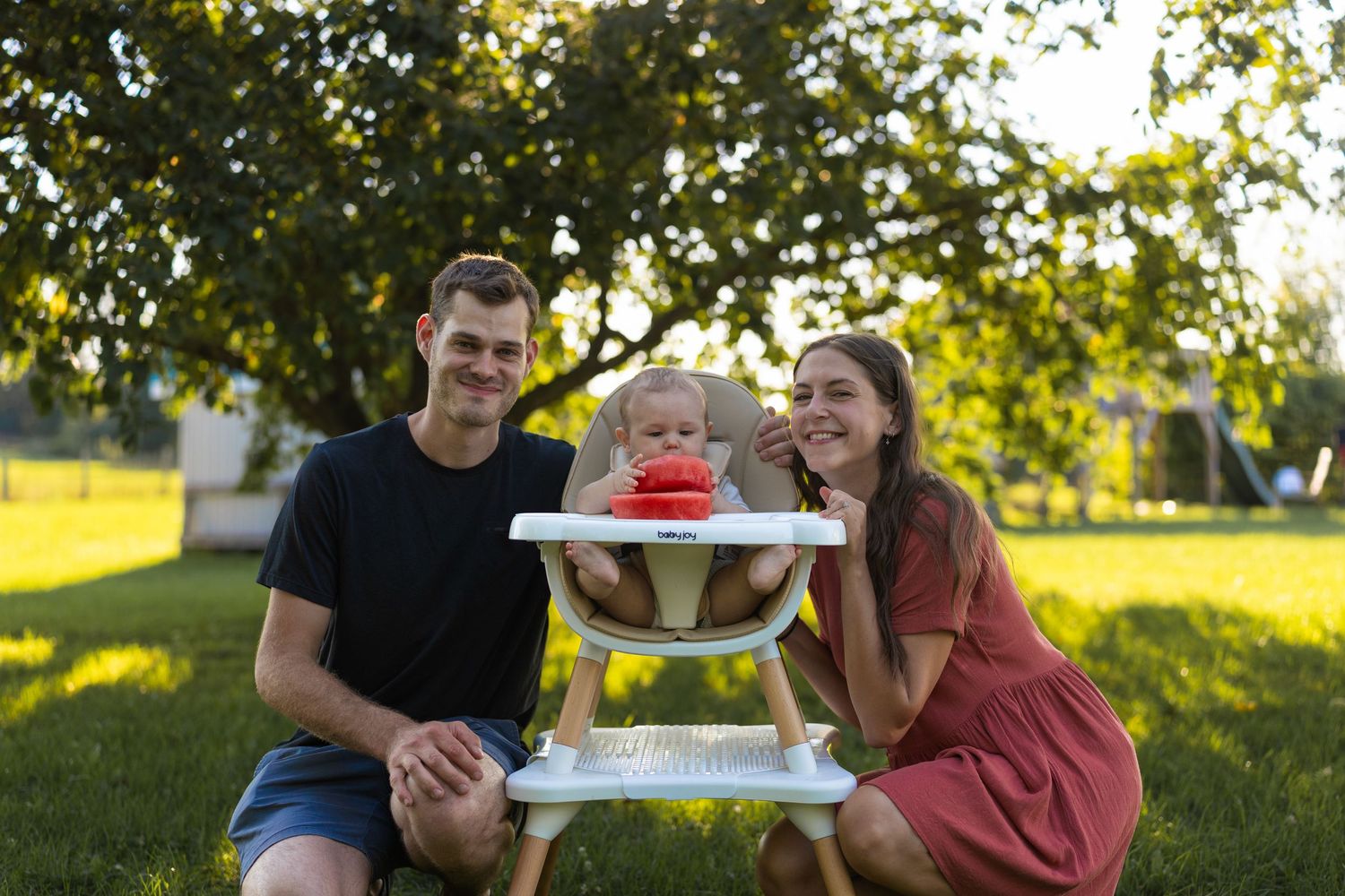 Young family with baby in high chair enjoying sunny day outdoors on green grass.