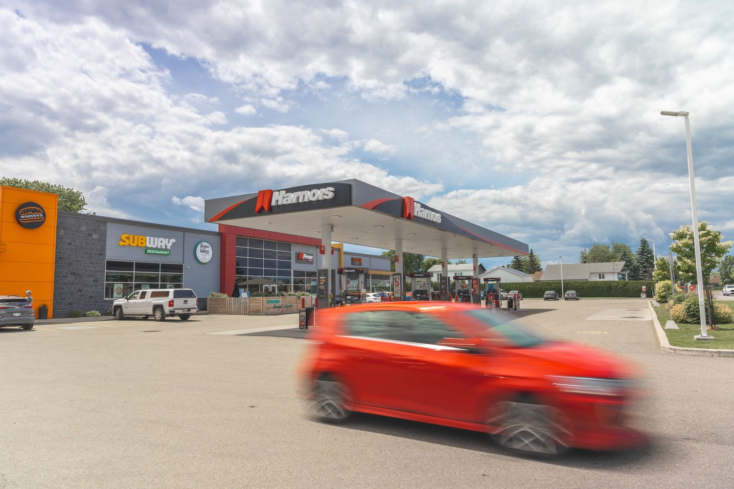 A bright red sports car speeds past a modern commercial building complex with glass windows and metal siding.