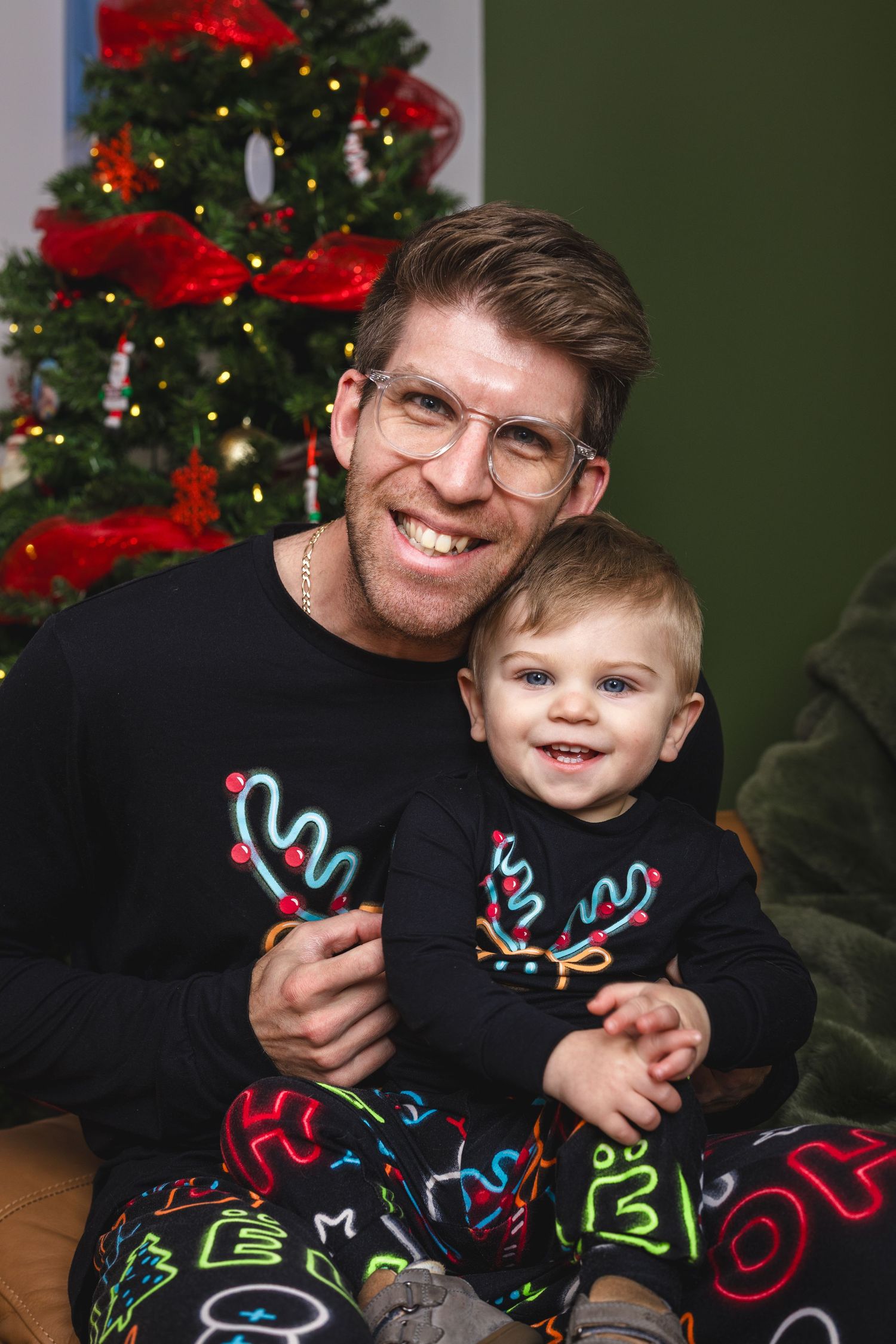 Festive holiday portraits with matching Christmas sweaters in front of decorated tree.