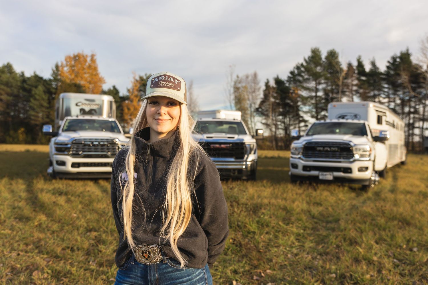 Row of parked vehicles and trailers in an autumn field setting.