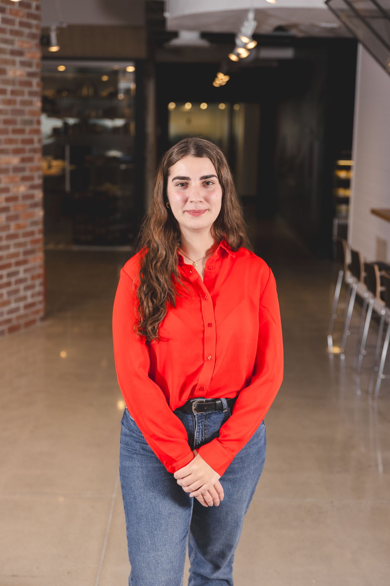 Professional in red button-down shirt and jeans standing in industrial-style office space.