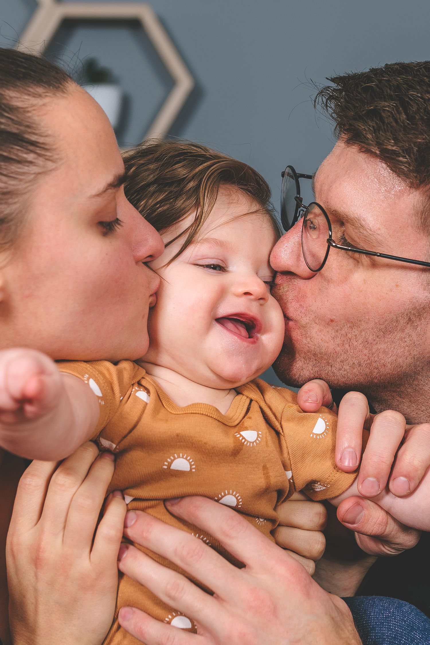 Loving family moment sharing kisses and cuddles while wearing matching outfits against blue backdrop.