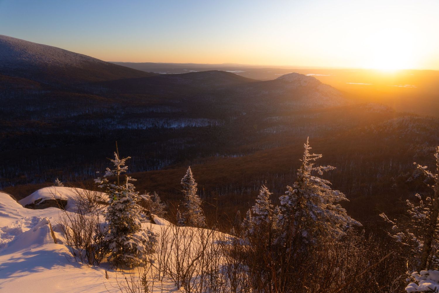 Snow-covered mountain peaks silhouetted against a dramatic sunset sky in winter.
