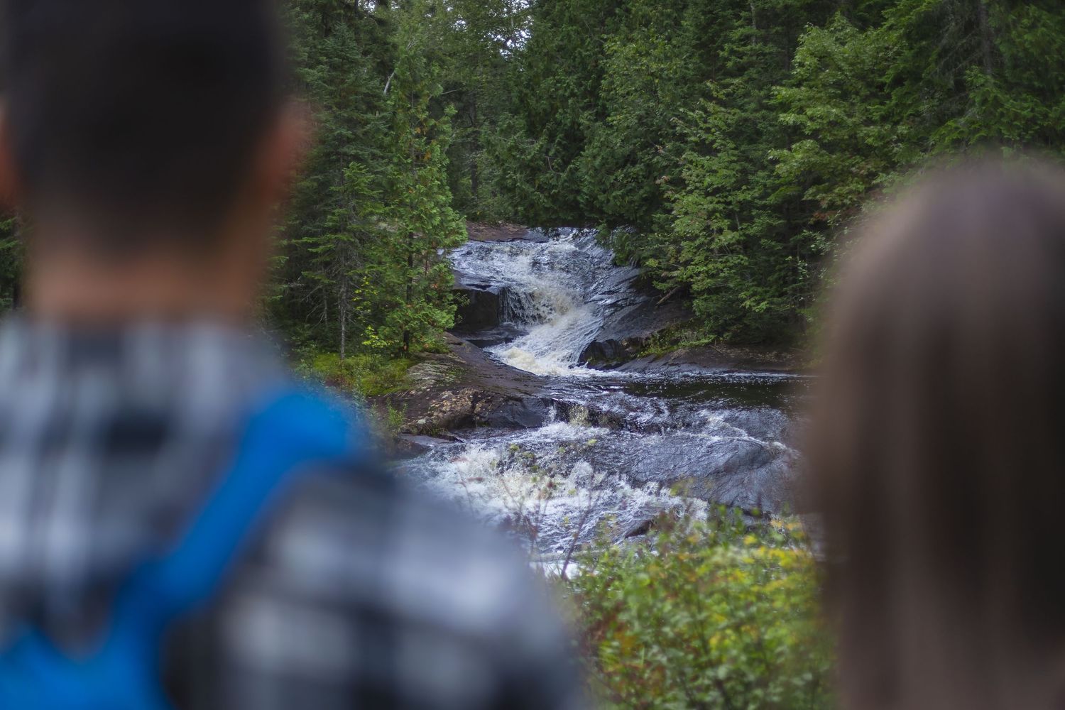 Natural waterfall flowing through forest with visitors observing.