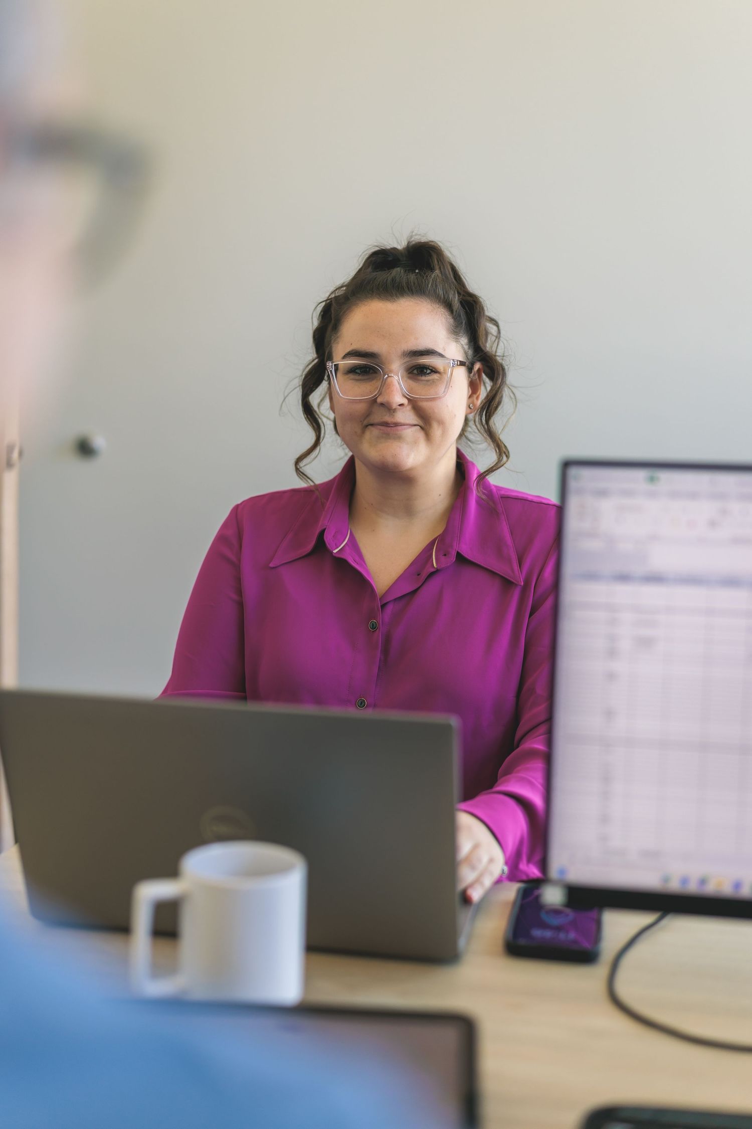 Office worker in magenta blouse works on laptop during meeting.