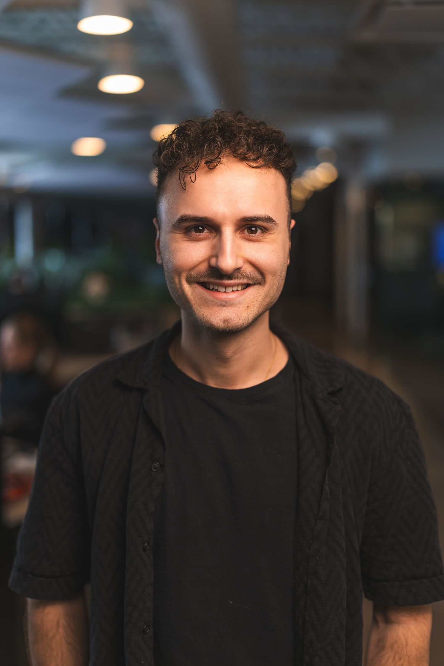 Person in black shirt smiling at camera in indoor office environment.