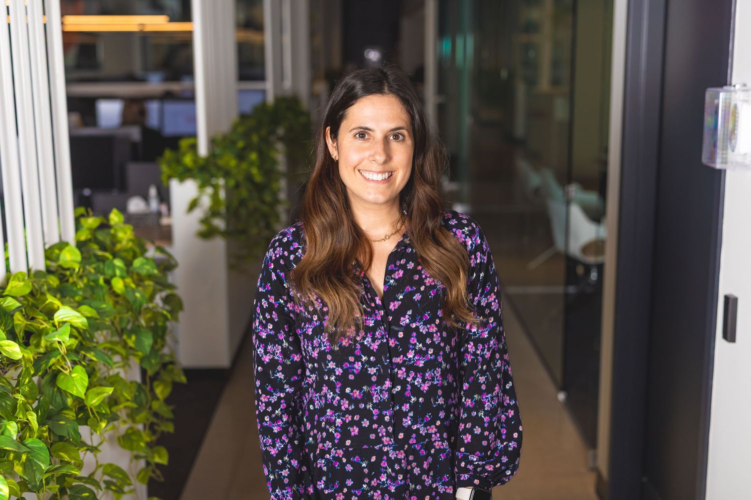 Professional headshot of employee in front of indoor plants and office windows.