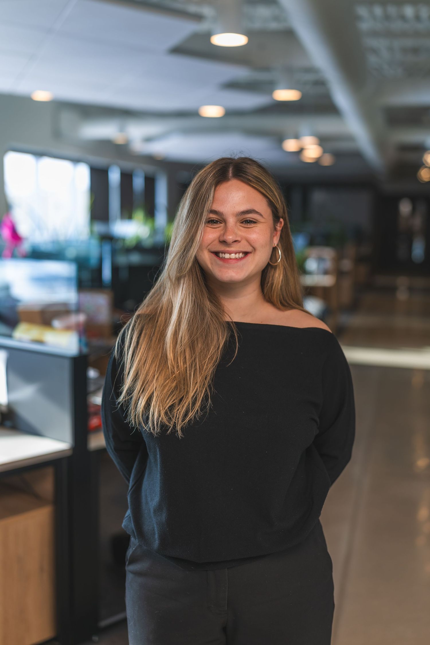 Professional in black top smiling in modern office environment with overhead lighting.