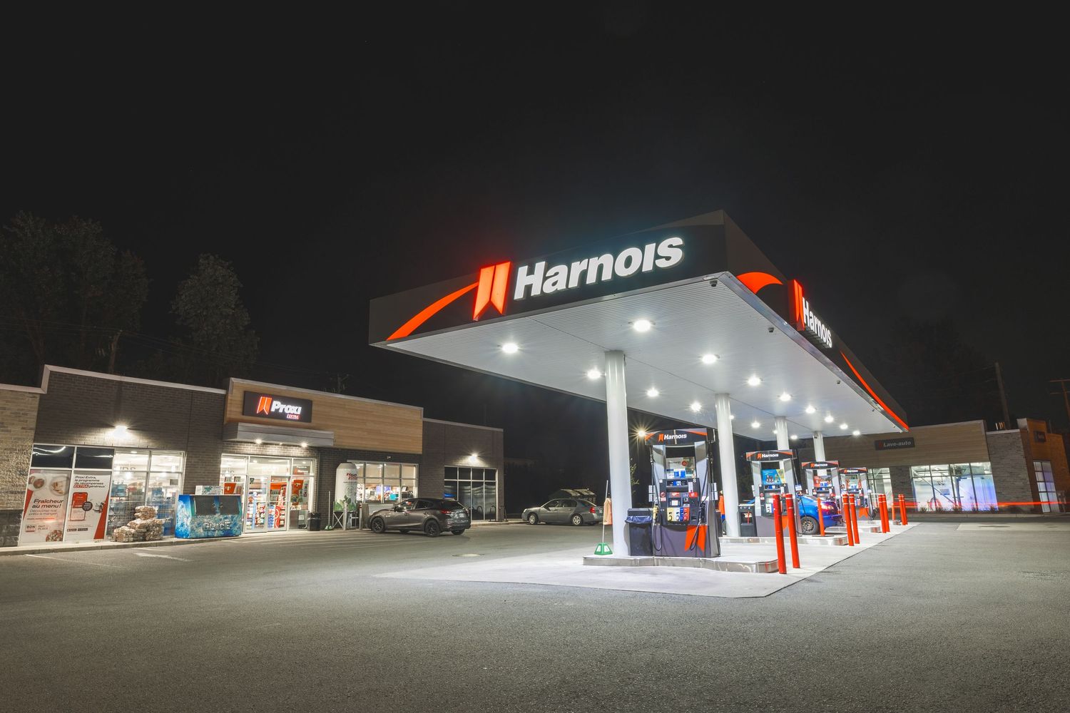 Gas station illuminated at night with bright red signage and white canopy extending over fuel pumps.