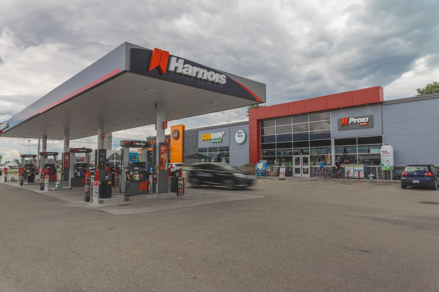 Modern gas station and convenience store exterior with red accents and multiple fuel pumps under a large canopy.