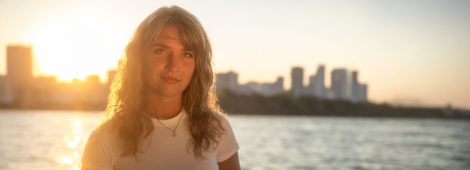 Person posing near waterfront during golden hour sunset.