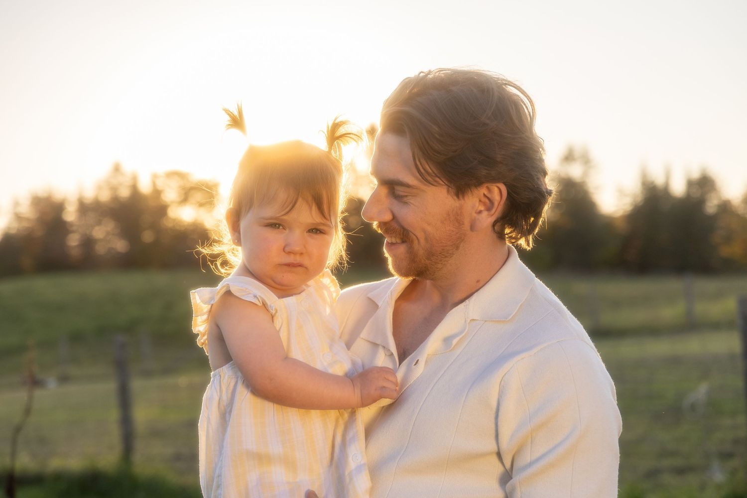 Family shares tender embrace while wearing white during outdoor sunset photo session.