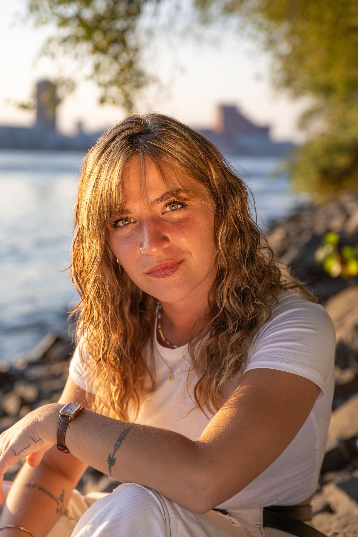 Portrait of person in white t-shirt at sunset near rocky waterfront.