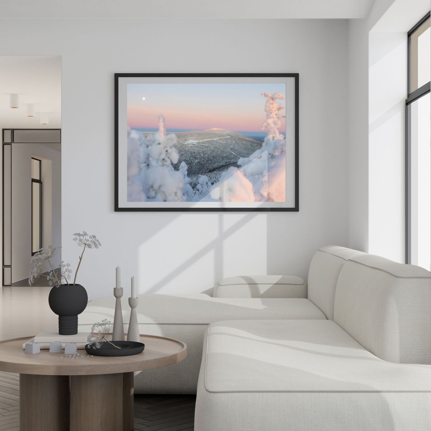 Modern minimalist living room interior with white furniture and framed landscape artwork.