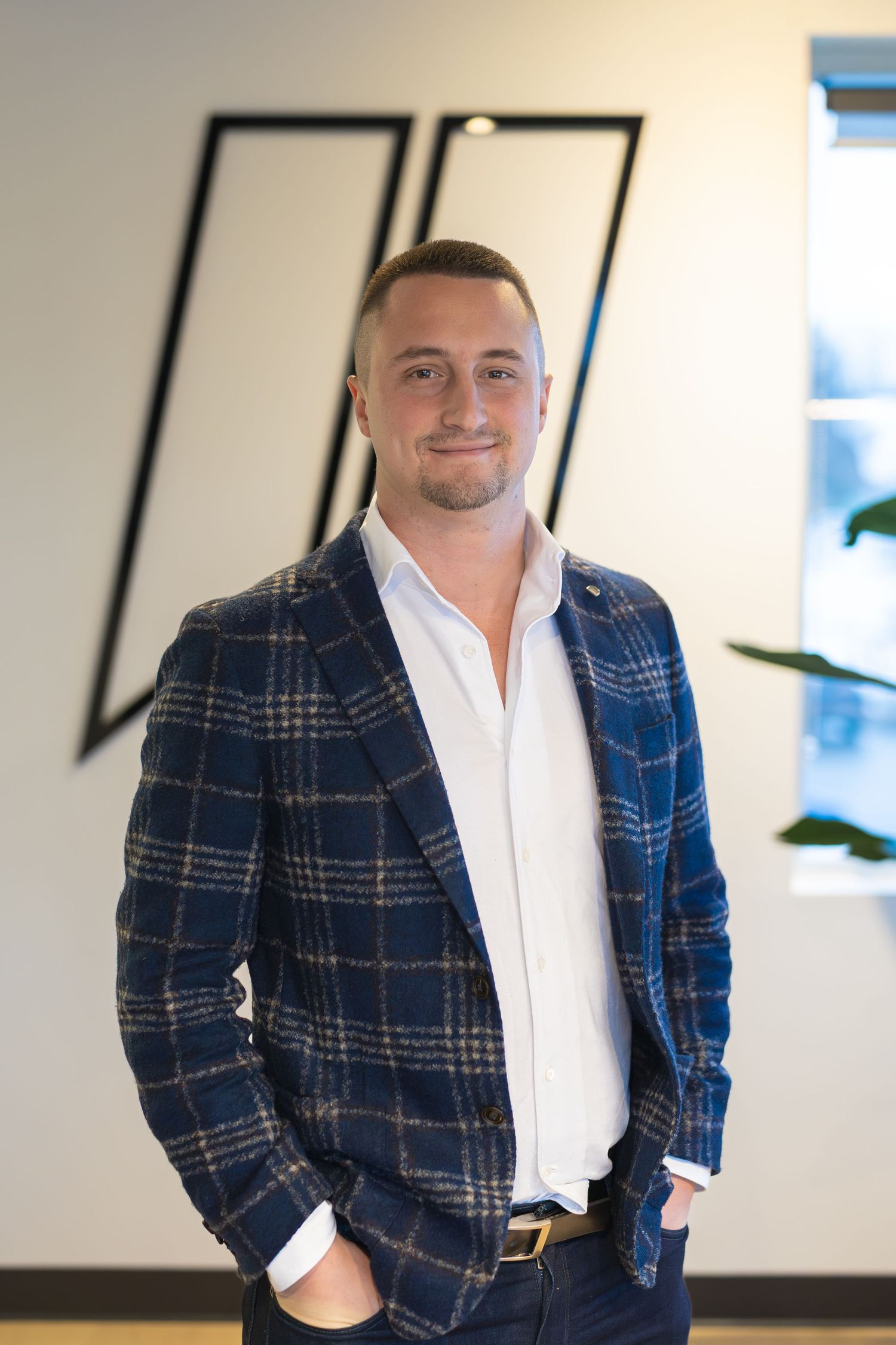 Professional portrait of person wearing navy plaid blazer and white shirt in modern office setting.