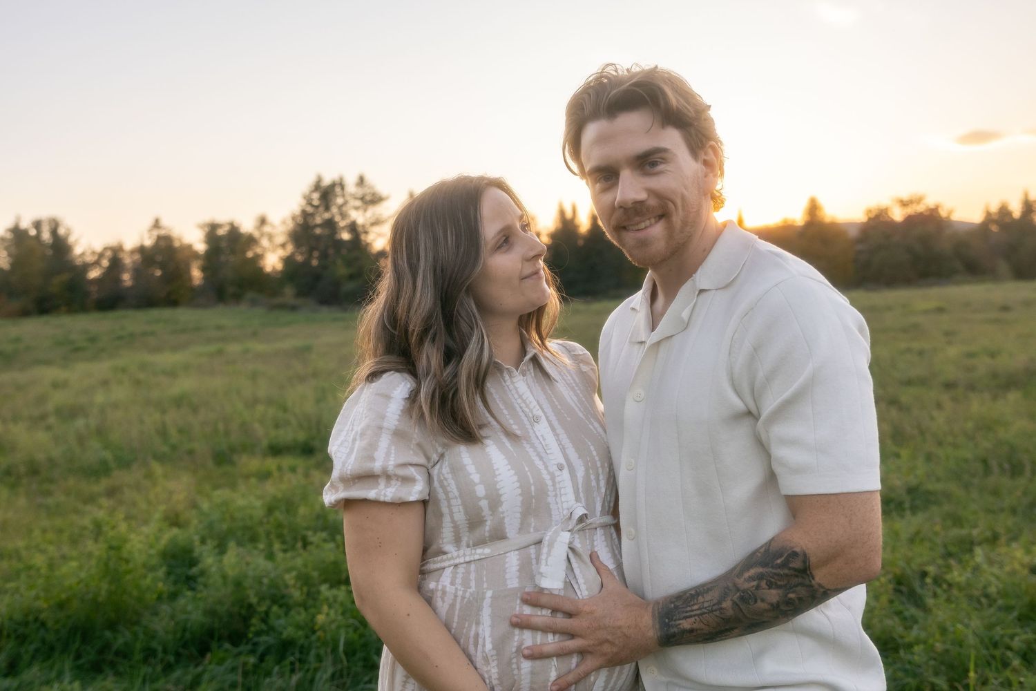 Casual family portrait session in white outfits against scenic rural landscape at golden hour.