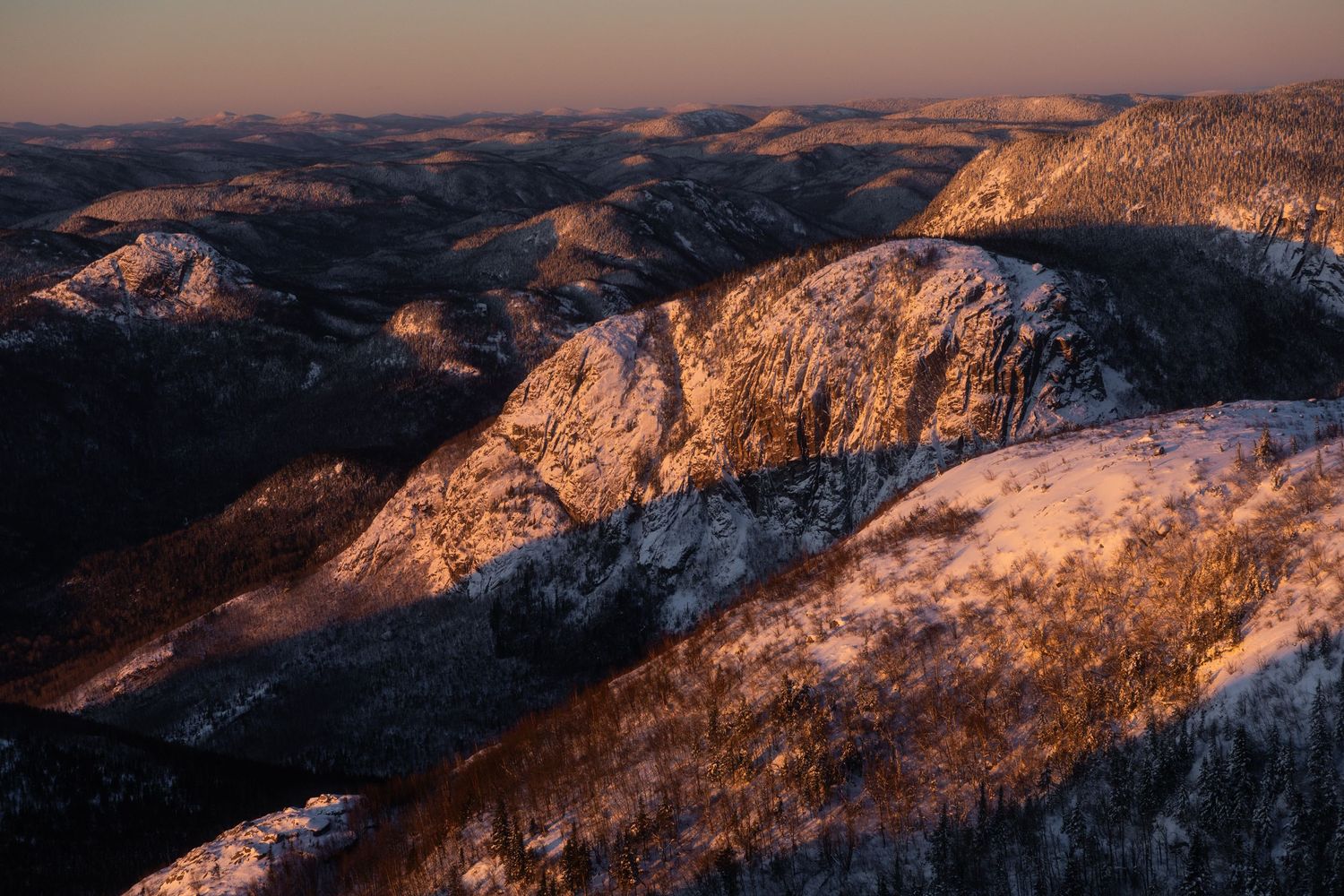 Snow-capped mountain peaks illuminated by golden sunlight at dusk.