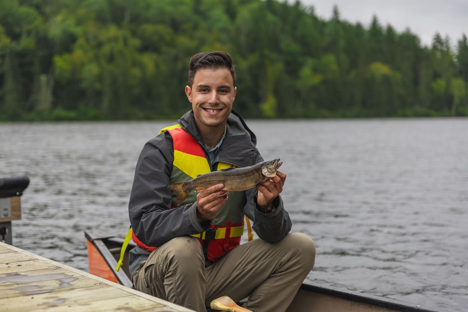 People fishing from kayaks on a scenic lake surrounded by evergreen forest.