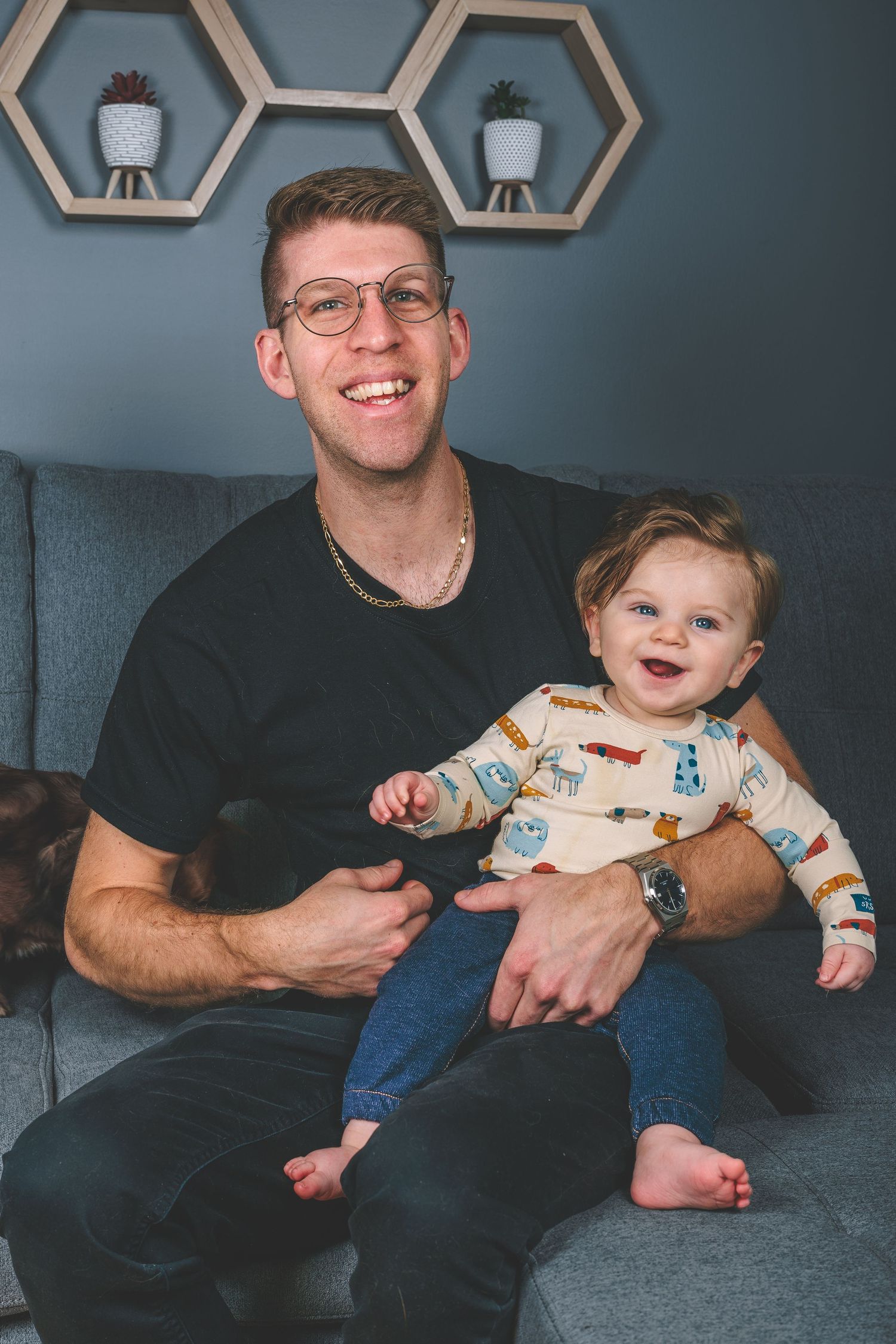 A parent and child share a cheerful moment on a gray couch with hexagonal wall decorations.