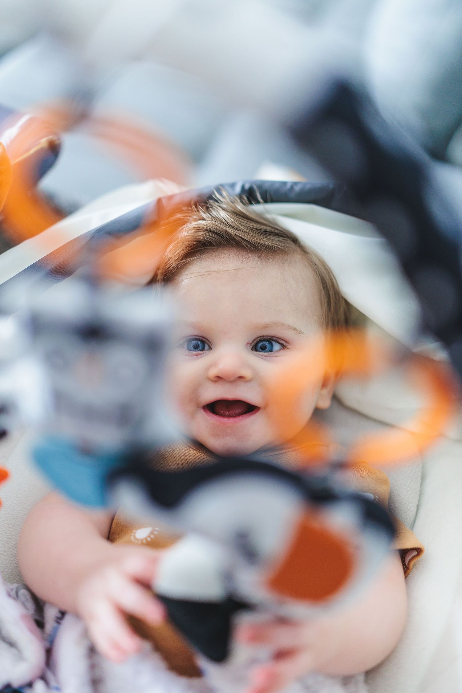 A smiling baby with striking blue eyes photographed through artistic orange bokeh effects.