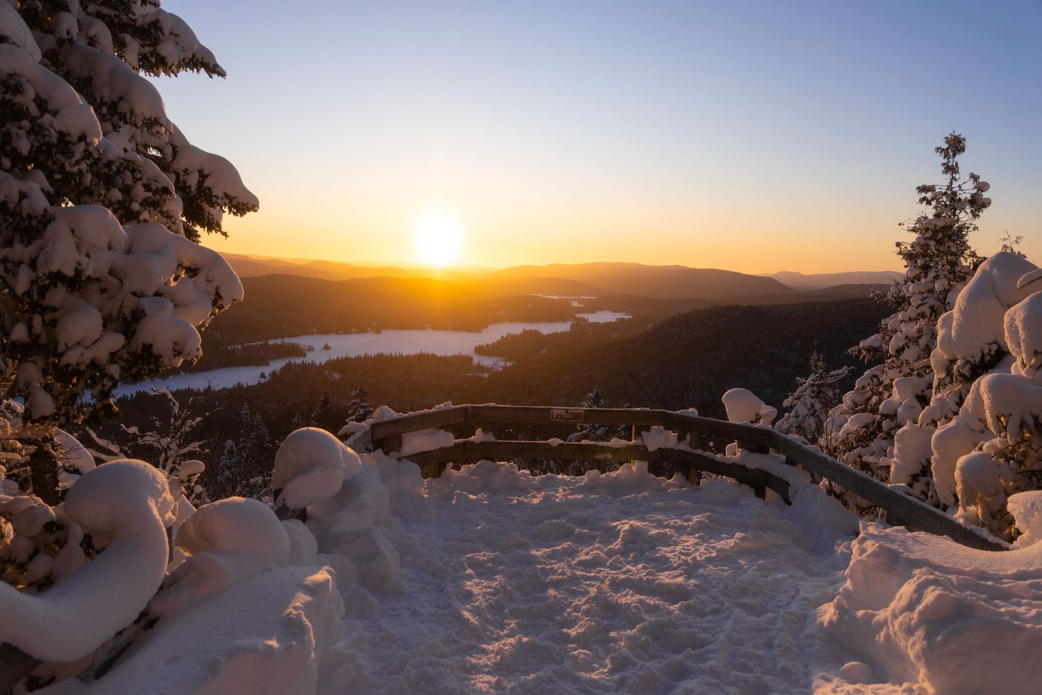 Panoramic view of a snowy mountain landscape at sunset with ice-encrusted trees.