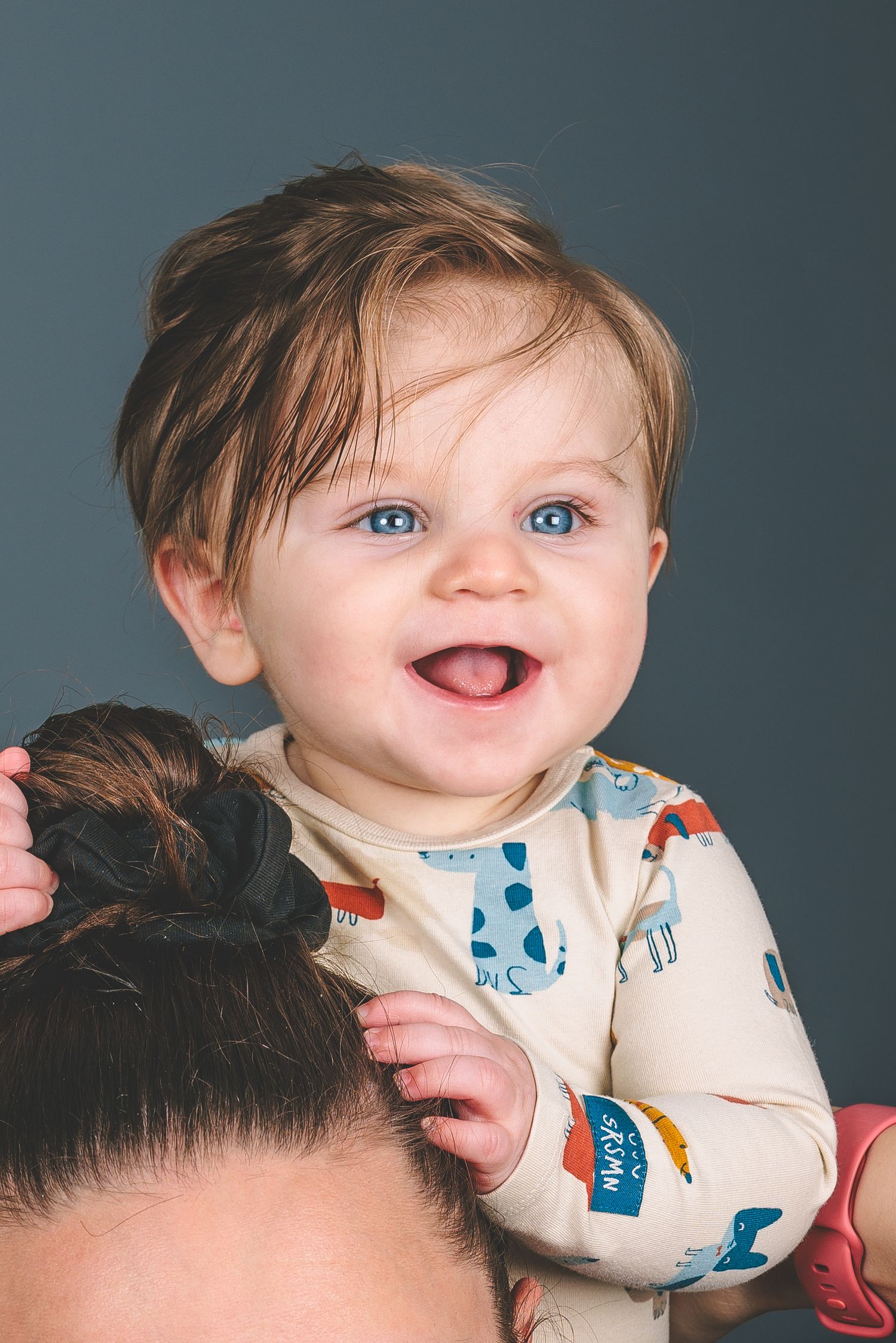 A bright-eyed baby with a big smile wearing a patterned onesie.